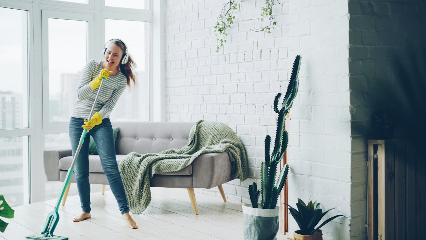 Woman wearing yellow gloves mops a wooden floor while singing.