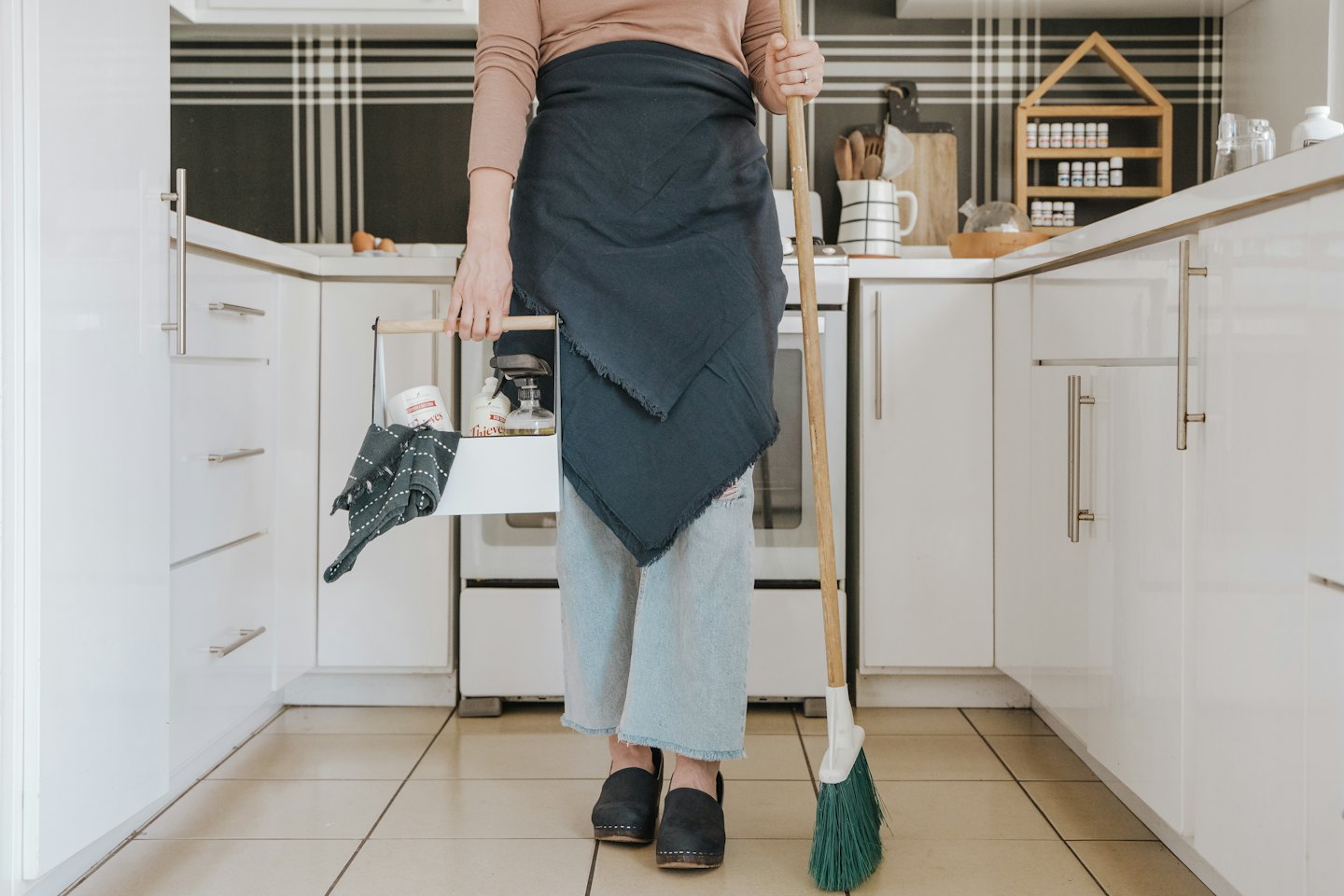Woman holding cleaning supplies in a bright, modern kitchen.