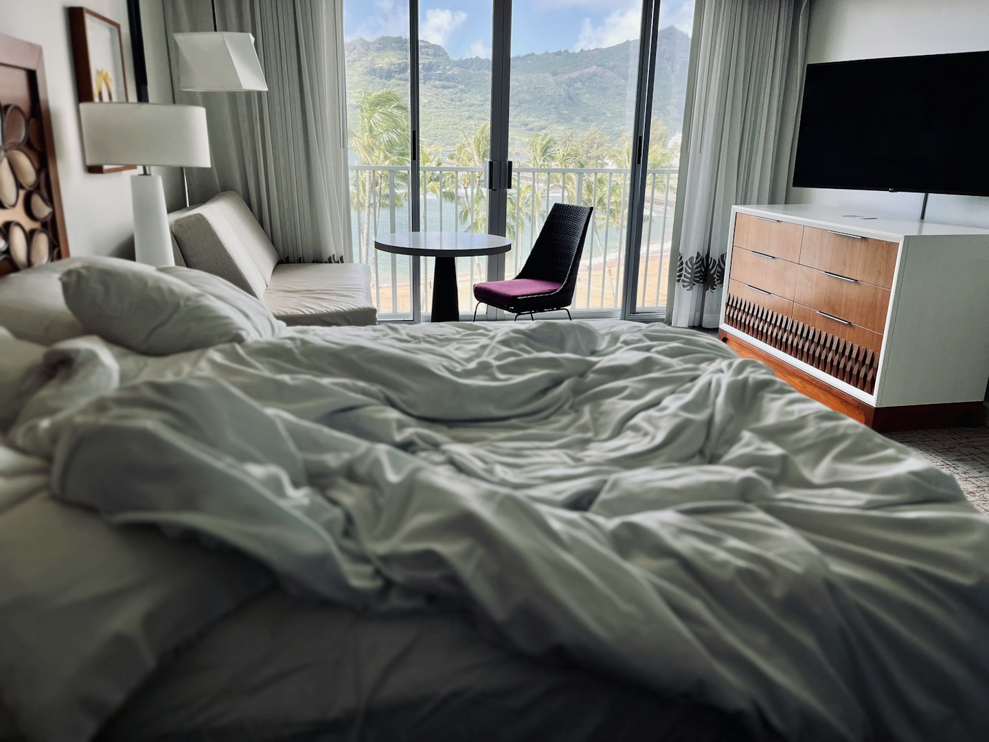 Rumpled hotel bed overlooking a balcony with mountain and ocean views.